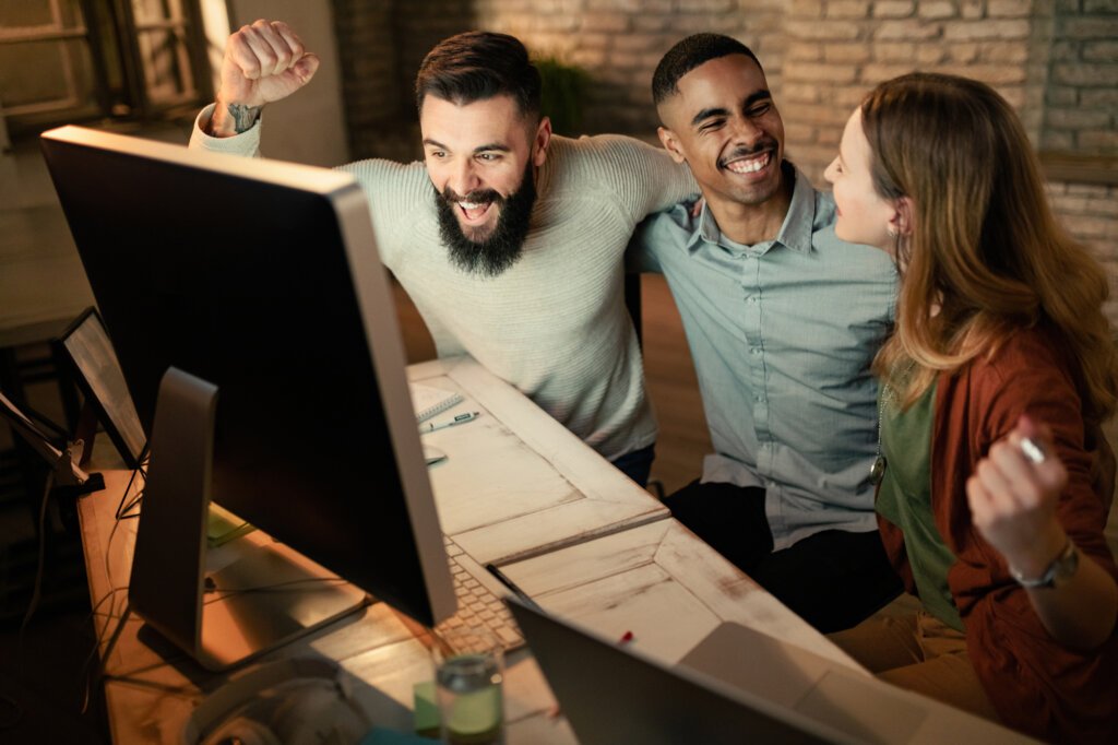equipe de inicializacao jovem comemorando o sucesso dos negocios enquanto usa o computador no escritorio